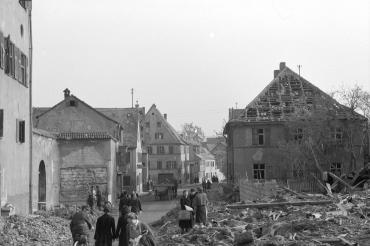 April 1945: Ein Blick in die zerstörte Pflegstraße in Donauwörth mit Passanten, gegenüber dem Fuggerhaus auf der linken Seite liegen die Trümmer des zerstörten Eckhauses. 