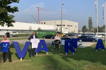 Drei Männer mit Trikots bei Logo der Varta AG