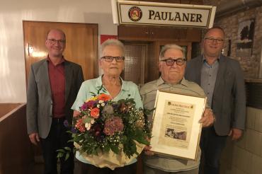 Drei Männer und eine Frau in Gastwirtschaft, Frau mit Blumen, Mann mit Urkunde