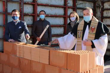 Vier Personen mit Maske legen Grundstein auf Baustelle