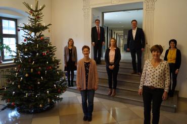 Sieben Personen stehen mit Abstand neben einem Weihnachtsbaum