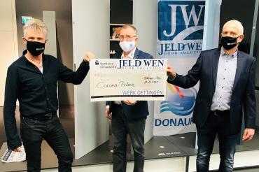 Drei Männer mit Mundschutz und Scheck vor Jeld-Wen-Banner