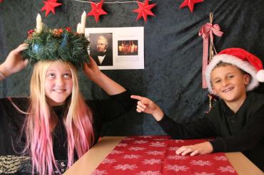 Mädchen mit Adventskranz auf dem Kopf, daneben Junge mit Weihnachtsmütze