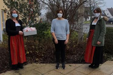 Drei Frauen mit Masken, zwei davon in Tracht