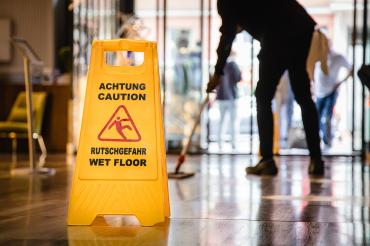 Schild Vorsicht Rutschgefahr, dahinter Gebäudereiniger beim Bodenwischen