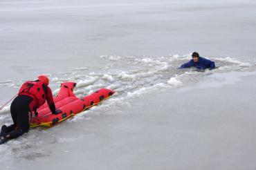 Das Bild zeigt einen Retter der DLRG, der sich mit einem aufblasbaren Eisrettungsschlitten zu einer eingebrochen Person vorarbeitet.