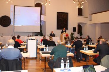 Stadträte sitzen im Stadtsaal Klösterle, vorne Leinwand und David Wittner am Pult