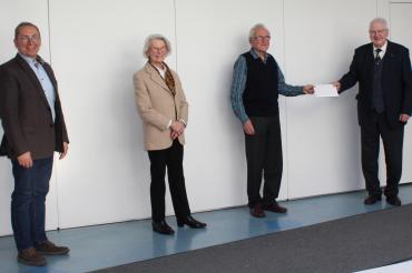 Vier Personen vor weißer Wand bei Spendenübergabe