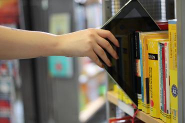 Das Bild zeigt ein Tablet in einem Bücherregal. 