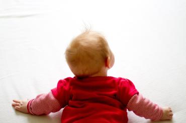 Das Bild zeigt ein Baby wie es krabbelt und hoch schaut. 