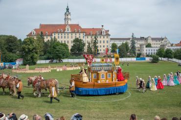Das Bild zeigt eine Parade von Menschen, die mit barocken Kleidern anzogen sind.