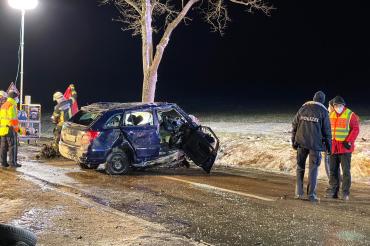 Unfallwagen steht auf Straße, dabei Polizisten und Feuerwehrleute