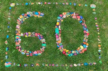 Das Bild zeigt angemalte Steine, die zu der Zahl 60 arrangiert wurden. 
