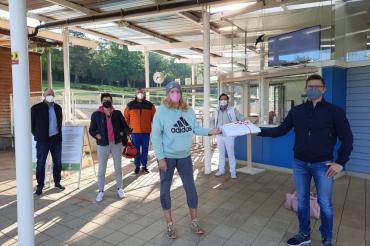 Der Bürgermeister überreicht der ersten Besucherin ein Handtuch. Im Hintergrund sind vier weitere Badegäste zu sehen.