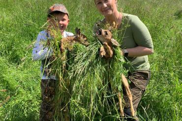 Ein Junge und eine Frau halten zwei Rehkitze in den Händen. 