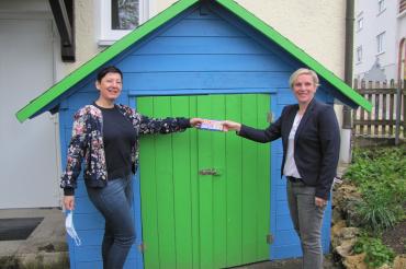 Das Bild zeigt die Familienbeauftragte des Landkreises Donau-Ries, Ursula Leinfelder (rechts) bei der Übergabe einer kleinen Aufmerksamkeit an Birgit Bayer, Leitung des Kindergarten St. Johannes in Rögling (links)