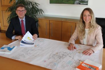 Das Bild zeigt Stefan Rößle mit Barbara Wunder am Tisch mit einem Bauplan. 