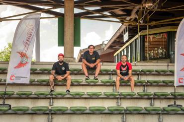 Drei Männer sitzen auf Stadiontribüne