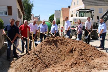 Zehn Personen mit Spaten hinter Sandhaufen