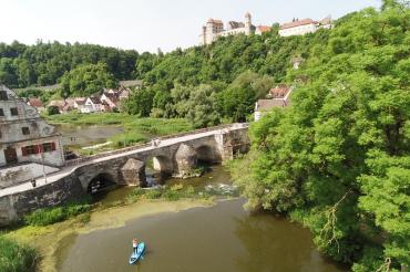 Wörnitz mit Steinerner Brücke, Stand-Up-Paddlerin auf dem Wasser, im Hintergrund die Harburg