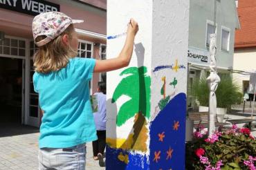 Kind steht auf kleiner Leiter und bemalt weiße Säule