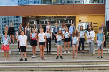 Kinder mit Urkunden und Schulleiter vor Schuleingang