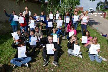 Auf dem Bild sind die Schüler*innen der dritten und vierten Klasse zu sehen. Neben einer Urkunde haben sie außerdem eine süße Belohnung erhalten. 