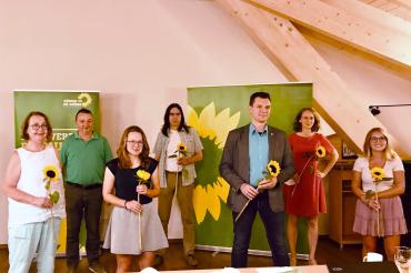 Acht Personen mit Sonnenblumen vor Roll-Ups von Bündnis90/Die Grünen