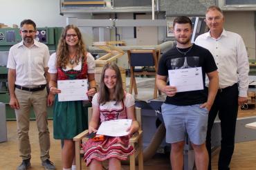 Zwei Schülerinnen in Tracht, ein Schüler und zwei Lehrkräfte in einer Werkstatt