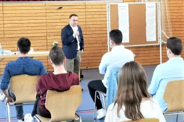 MdB Lange steht mit Mikrofon vor fünf Personen, die mit dem Rücken zum Bild sitzen