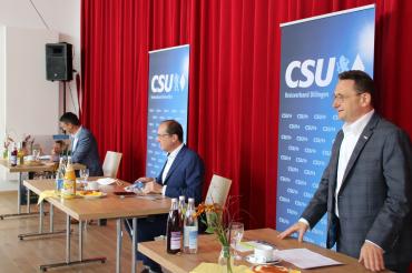Drei Herren im Anzug an drei Tischen vor CSU-Roll-ups und rotem Vorhang
