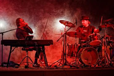 Keyboarder und Schlagzeuger auf Bühne in rot-lila Licht und Nebel