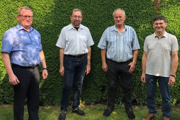 Vier Männer stehen vor einer Hecke