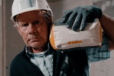 Bauarbeiter im Rentenalter schleppt Sack Zement auf der Schulter