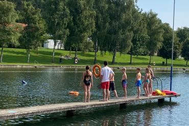 Auf dem Bild zu sehen die Kinder am Wasser mit Rettungsringen.