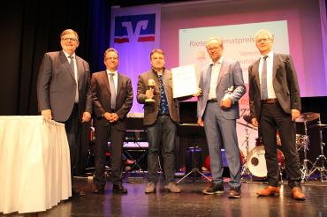 Die Preisverleihung an Dr. Oliver Sachs (Mitte), mit Paul W. Ritter (Vorstandsvorsitzender RVB Ries eG, links), Prof. Dr. Markus Glück, (Aufsichtsratsvorsitzender, 2. von links), Prof. Dr. Kai Wünnemann (Laudator, 4. von links) und Bernhard Ströbele (stellvertretender Vorstandsvorsitzender, rechts).