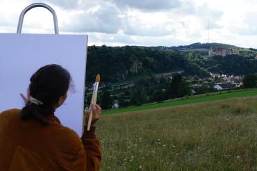 Auf dem Bild zu sehen eine Staffelei vor der Burg Harburg.