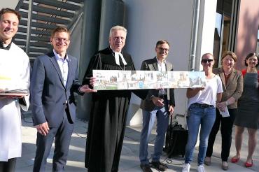 von links nach rechts Diakon Roland Kiechle, OB David Wittner, Dekan Gerhard Wolfermann hält zusammen mit Architekt Michael Leberzammer die Bildleiste die den Umbau dokumentiert, KiGa-Leiterin Annika Schneider, stv. Landrätin Claudia Marb, Präsidiumsmitglied KV Kathrin Wagner nach der Einweihungsfeier zur Erweiterung des Montessori-Kinderhauses am Nördlinger Kastanienbaum