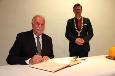 Hermann Faul sitzt an Tisch und trägt sich in Goldenes Buch der Stadt ein, dahinter steht OB David Wittner