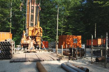 Brunnenbohrgerät mit Werkzeugen darum, dahinter Bäume