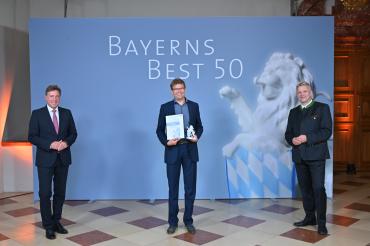 Das Foto zeigt (von links nach rechts) Prof. Dr. Thomas Edenhofer, Partner der Kanzlei Baker Tilly (Juror), Jürgen Schuster, Geschäftsführer der Raumschmiede GmbH, sowie Roland Weigert, Staatssekretär im Bayerischen Wirtschaftsministerium, bei der Preisverleihung.