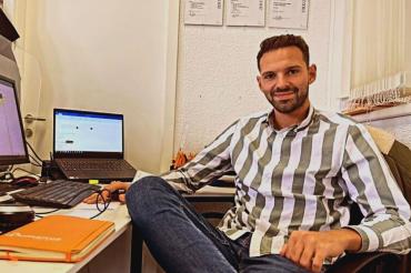 Astrit Shkodriqi an Schreibtisch mit Bildschirmen