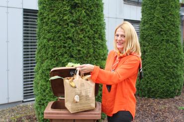 Auf dem Bild ist eine Frau abgebildet, die ihren Müll in der Biotonne entsorgt. 