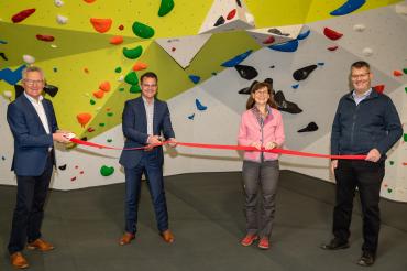 Vier Personen vor Boulderwand halten rotes Band