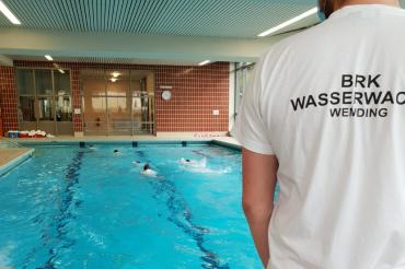 Mann mit T-Shirt-Aufdruck BRK Wasserwacht Wemding steht an Rand eines Beckens im Hallenbad