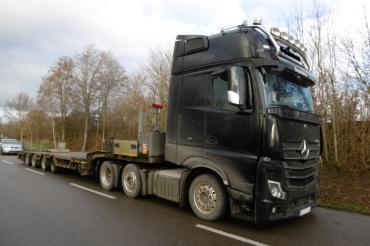 Schwarzer Sattelzug mit Tiefbettschwertransportauflieger steht am Straßenrand