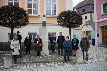 Das Bild zeigt die Teilnehmenden der Gedenkveranstaltung, darunter: vorne links Stadträtin Andrea Eireiner, zweite links von der Stele Kreisvorsitzende Elisa Pfaff, links neben der Stele die 1. Vorsitzende des Freundeskreis Synagoge Hainsfahrt e.V. Sigi Atzmon, rechts von der Stele der Bezirksrat der Grünen und Donauwörther Stadtrat Albert Riedelsheimer.