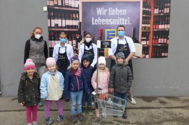 Zu sehen sind Mitarbeiter des Edeka-Marktes und die Kinder der Tagesstätte bei der Übergabe des Einkaufswagens. 