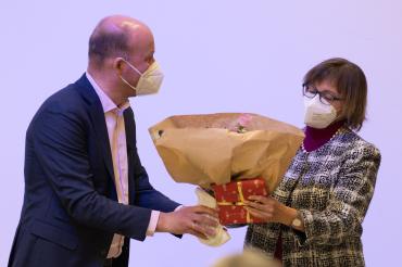 Blumen und ein verpacktes Geschenk werden an Dr. Ruth Kilian übergeben.