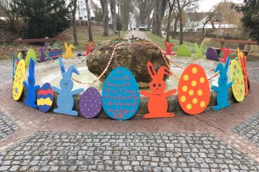 Ein mit bemalten Hasen und Ostereiern aus OSB-Platten verzierter Springbrunnen.